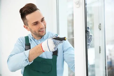 Construction worker adjusting installed window with screwdriver indoors Stock Photos