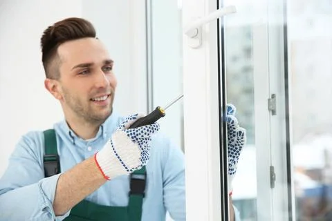 Construction worker adjusting installed window with screwdriver indoors Stock Photos