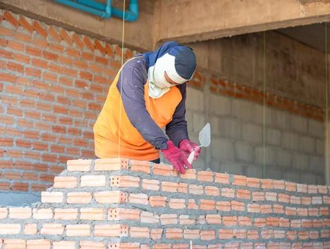 A construction worker and bricklayer meticulously laying orange clay bricks.. Stock Photos
