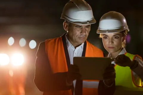 Construction worker and engineer using digital tablet at dark construction site Stock Photos