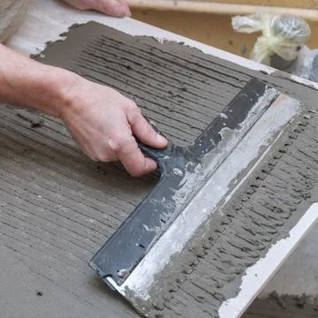 A construction worker applies cement to ceramic tile with a spatula Stock-Fotos