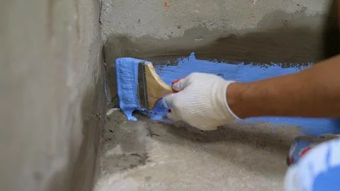 Construction worker applying blue waterproofing paint on concrete wall Stock Photos