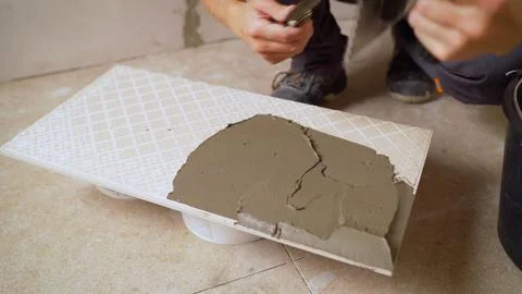 Construction worker applying cement glue to ceramic tile using a spatula 스톡 사진