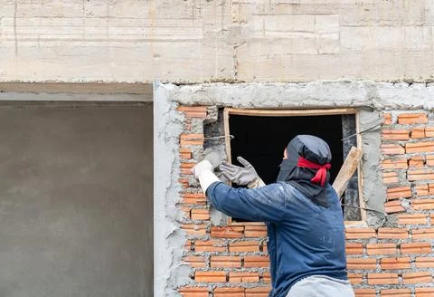 Construction worker applying cement mortar to a red brick wall around a win.. 库存照片