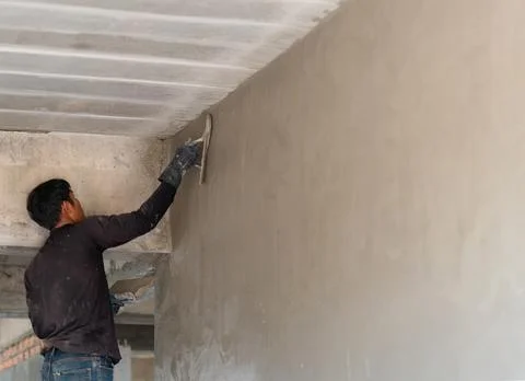 Construction worker applying cement plaster on an upper wall edge using a m.. Stock Photos