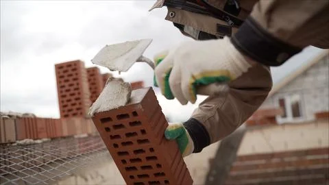 Construction worker applying cement with trowel on red brick during house b.. Stock Photos