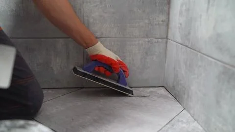 Construction worker applying grout to floor tiles in bathroom renovation Stock Photos