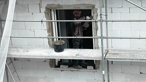 Construction worker applying plaster around window frame on scaffolding. Stock Footage 337985502