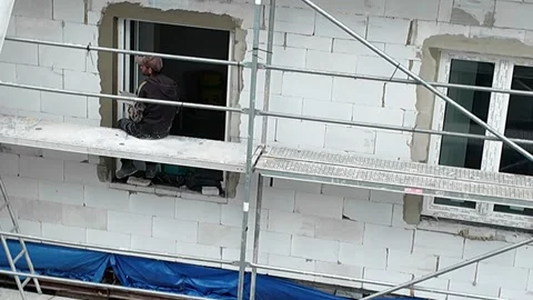 Construction worker applying plaster around window frame on scaffolding. Stock Footage 337985539