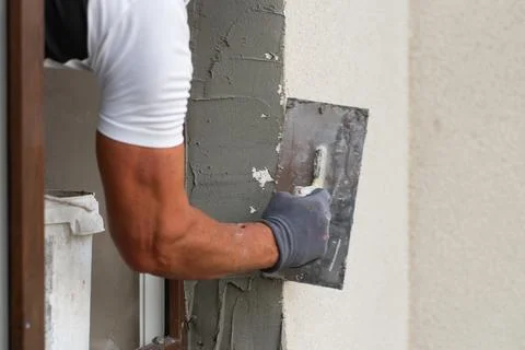 Construction worker applying plaster to a wall around a window during home Stock Photos