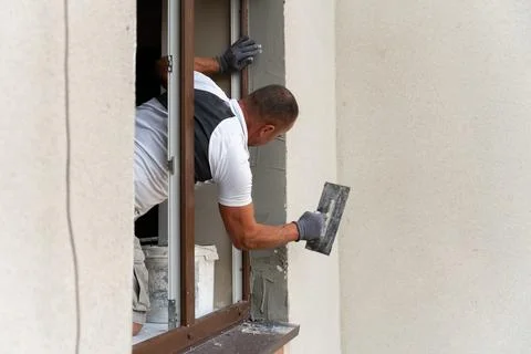 Construction worker applying plaster to a wall around a window during home Stock Photos