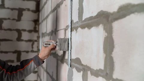 Construction worker applying plaster on white brick wall using trowel Stock Photos