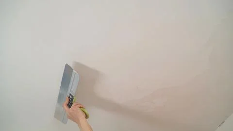 Construction worker applying plaster on white ceiling using spatula Stock Photos