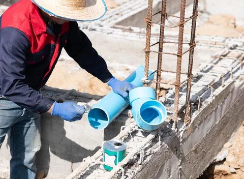 Construction worker applying PVC cement to blue plastic pipes for plumbing .. Foto stock