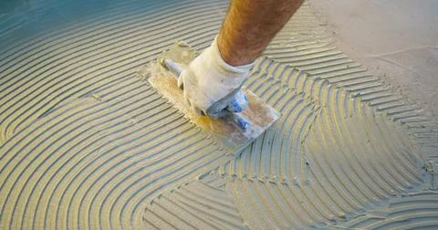 Construction worker applying tile adhesive to floor with notched trowel Stock Photos
