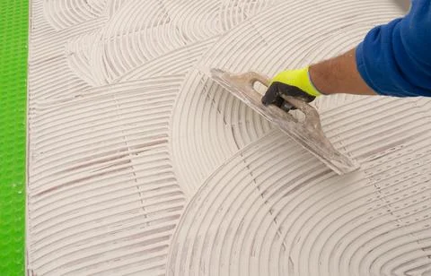 Construction worker applying tile adhesive to floor with notched trowel Stock Photos