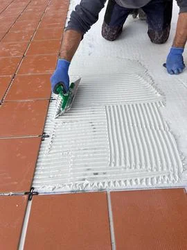 Construction worker applying tile adhesive to floor with notched trowel Stock Photos