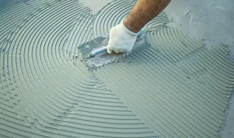 Construction worker applying tile adhesive to floor with notched trowel Stock Photos