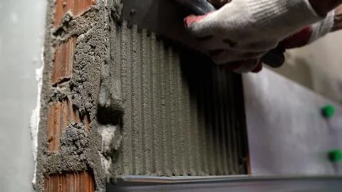 Construction worker applying tile adhesive to wall with notched trowel Stock Photos