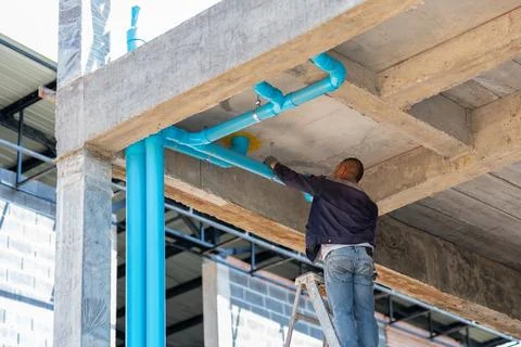 Construction worker attaching drainage and plumbing pipes to the ceiling st.. 스톡 사진