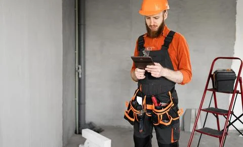 Construction worker bearded man in hardhat using digital tablet at constructi Stock Photos