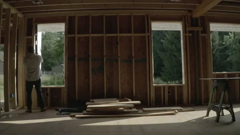 Construction Worker in Boots Checks Work with Level in Unfinished Home at Sunset Video stock 217655072