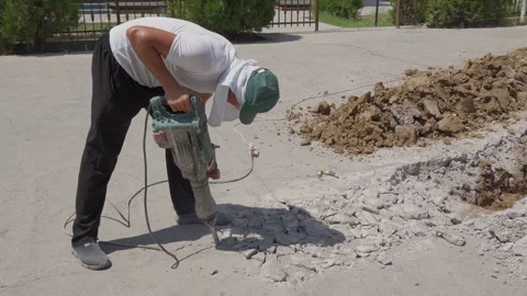 Construction worker breaking concrete pavement with an electric jackhammer Stock Footage 343395909