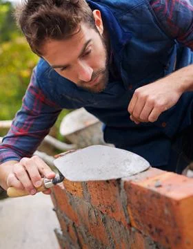 Construction worker, bricklayer and man building a brick wall, handyman or Stock Photos
