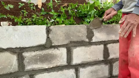 Construction worker building a concrete block wall in a garden setting Stock Footage 336097760