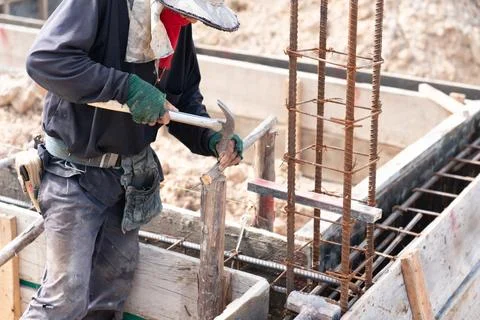 A construction worker at a building site is hammering a nail into wooden fo.. Stock Photos