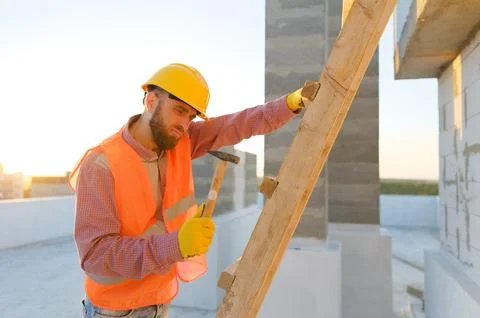 Construction worker building wooden structure on rooftop at sunset Stock Photos