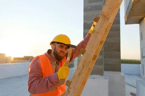 Construction worker building wooden structure on rooftop at sunset Stock Photos