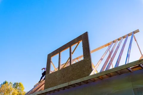 Construction worker builds roof structure with wooden beams in town environme Stock Photos