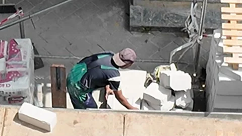 Construction worker carefully places building blocks on a sunny day Stock Footage 338332933