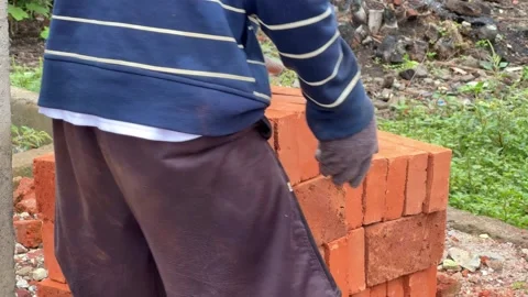 Construction worker carefully stacking red clay bricks at a building site. Stock Footage 321176338