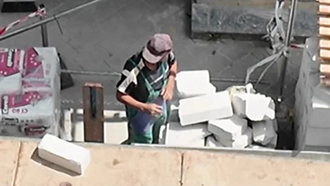 Construction worker carefully stacking white building blocks on a sunny day Stock Footage 338332938