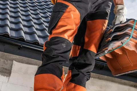 Construction Worker Carries Tiles While on a Roof During a Sunny Day at a B.. Stock Photos