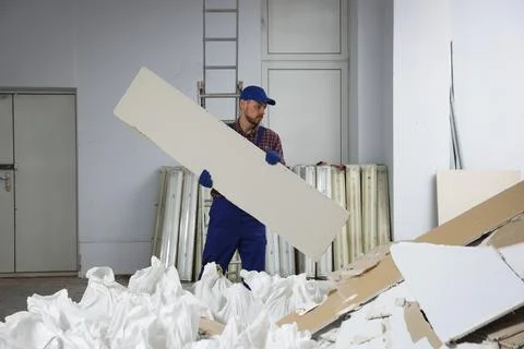Construction worker carrying used drywall in room prepared for renovation Stock Photos