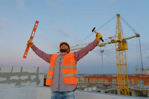 Construction worker celebrating with level and hammer at building site Stock Photos