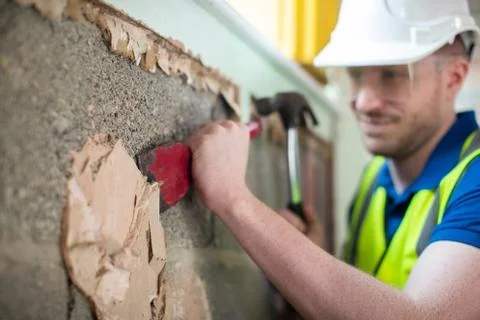 Construction Worker With Chisel Removing Plaster From Wall In Renovated House Stock Photos
