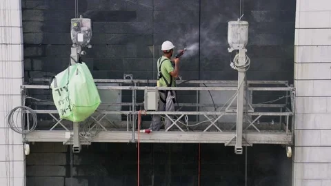 Construction worker cleans a wall of building using a high-pressure water spray Stock Footage