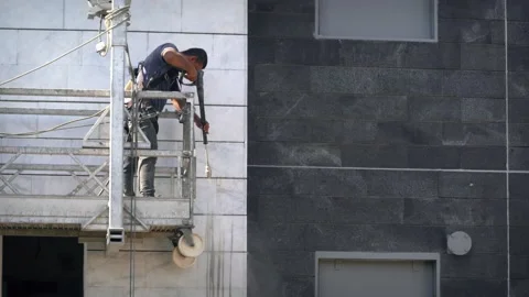Construction worker cleans a wall of building using a high-pressure water spray Stock Footage 134276821