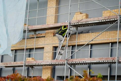 Construction worker climbing scaffolding at brick building Stock Photos