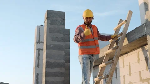 Construction worker climbs ladder at building site during daylight Stock Footage 286048630