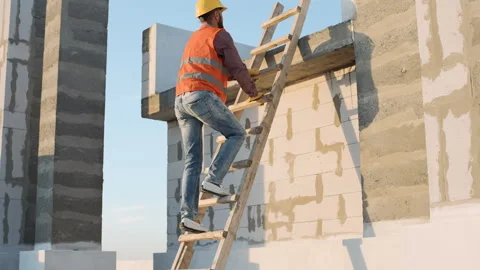Construction worker climbs ladder to inspect building structure at sunset Video stock 295958870