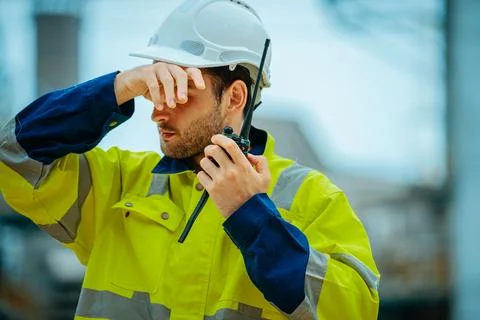 Construction worker communicating on radio while shielding eyes from sun at.. Stock Photos