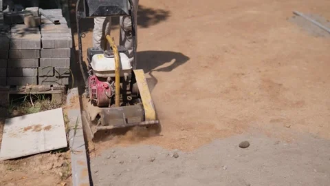 Construction worker with compacting machine beside stacked paving blocks on Stock Footage 344873744