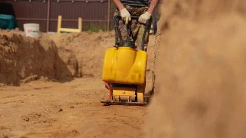 Construction worker compacting sand with plate compactor on building site Stock Photos