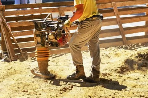 Construction worker compacting soil in house foundation using compactor. Wo.. Stock Photos