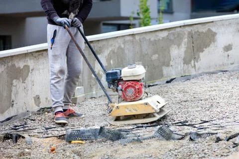 A construction worker compacts crushed stone with a petrol vibratory compacto Stock Photos